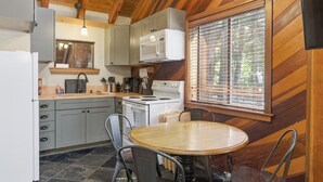 A kitchen with a stove, microwave, and cabinets, a dining table with chairs, and a window with blinds.