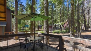 A wooden deck with a table and chairs, surrounded by a wooden fence, overlooking a forested area with tall trees.