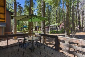 Eine Holzterrasse mit Tisch und Stühlen, umgeben von einem Holzzaun, mit Blick auf ein bewaldetes Gebiet mit hohen Bäumen.