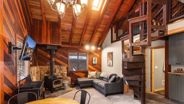L’intérieur chaleureux d’un chalet avec une cheminée en pierre, une table à manger en bois, un canapé et un téléviseur fixé au mur.