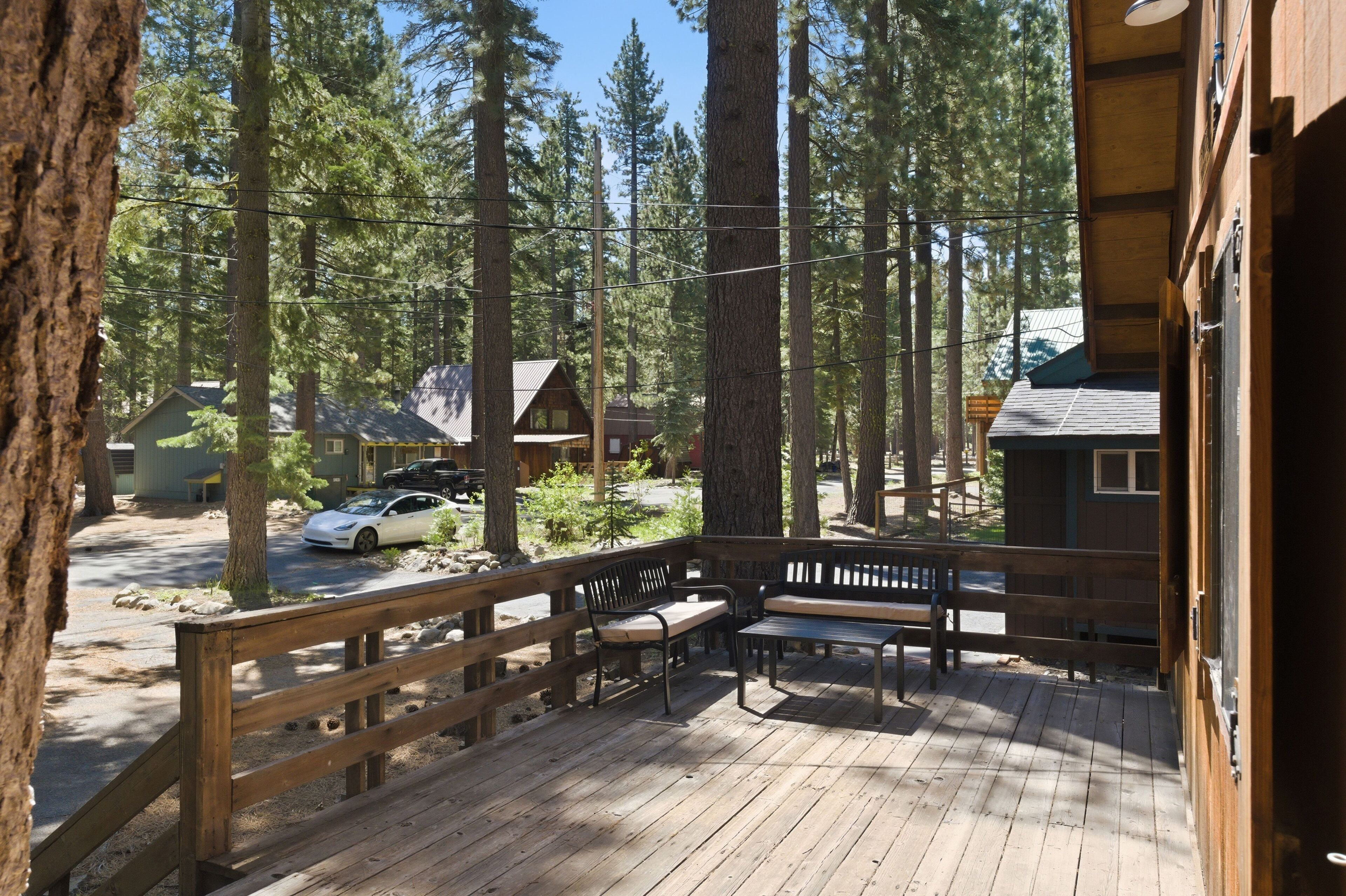 Un pontile in legno con panchine, circondato da alberi alti e un cottage sullo sfondo.