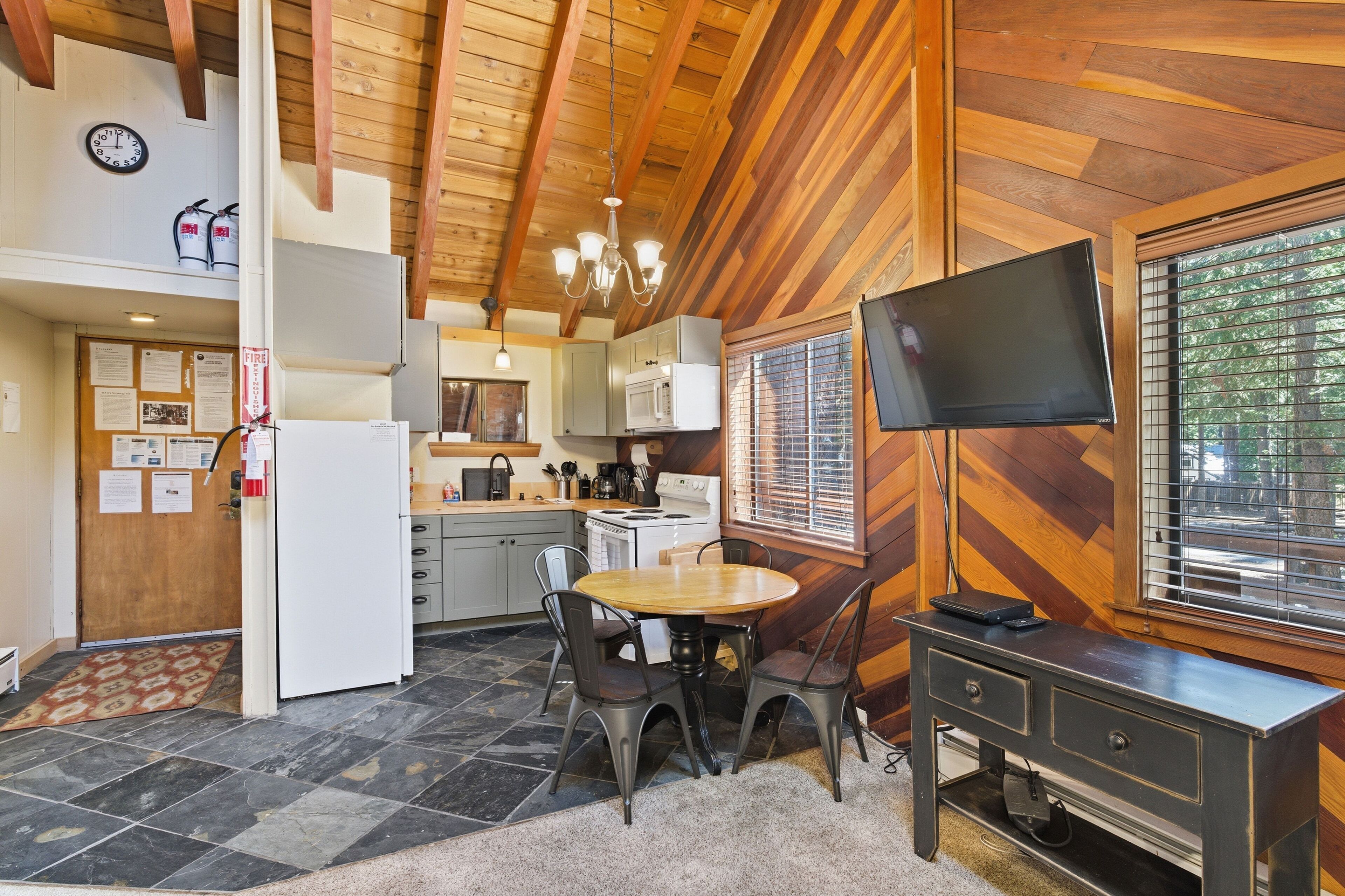 A kitchen with a dining table, chairs, a TV, and a window with blinds.
