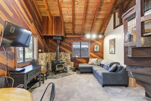 Ein gemütliches Blockhaus-Interieur mit Kamin, Fernseher, Sofa und Steinwand.