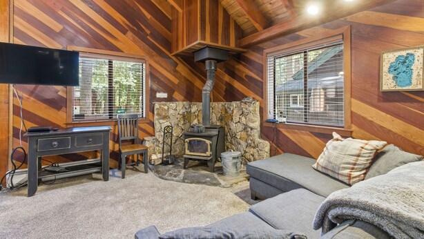 A cozy cabin interior with a stone fireplace, wooden walls, a sofa, a TV, and a desk.