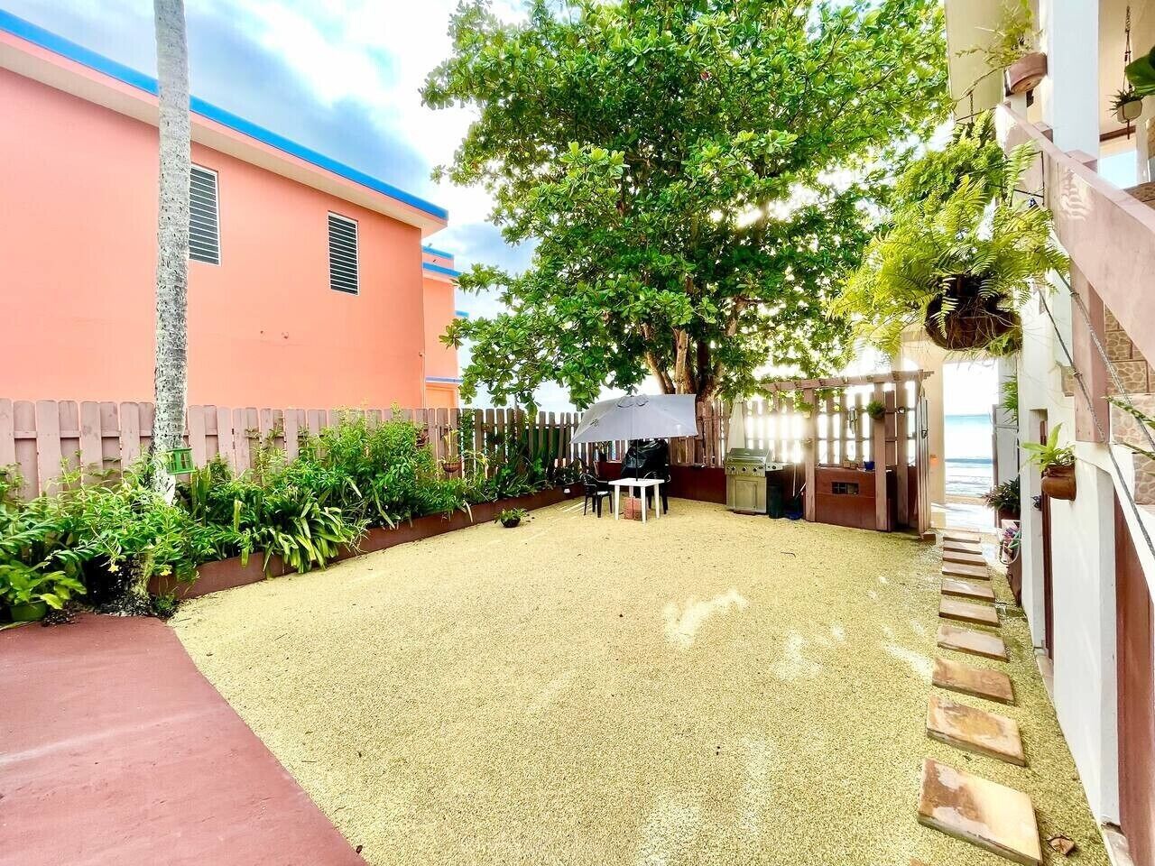 Un patio couvert, aménagé avec une table et des chaises, entouré d’une clôture et de plantes.