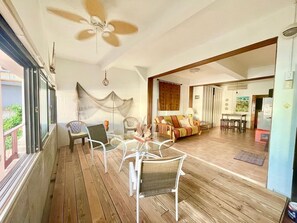 Ein geräumiger Balkon mit Deckenventilator, einem Glastisch mit Stühlen und einer Couch im angrenzenden Wohnbereich.