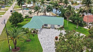 A residential property with a green roof, a paved driveway, and palm trees. - Palaco Paradise - Waterfront Oasis with Large Pool (Cape Coral)