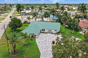 A residential property with a green roof, a paved driveway, and palm trees. - Palaco Paradise - Waterfront Oasis with Large Pool (Cape Coral)