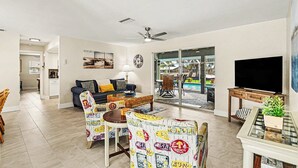 A living room with a sofa, chairs, a TV, and a dining area with chairs and a table. - Palaco Paradise - Waterfront Oasis with Large Pool (Cape Coral)