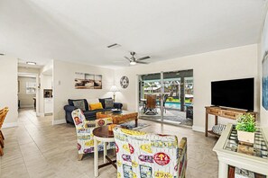 A living room with a sofa, chairs, a TV, and a dining area with chairs and a table. - Palaco Paradise - Waterfront Oasis with Large Pool (Cape Coral)
