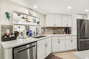 A modern kitchen with white cabinets, stainless steel appliances, a clock, and decorative wall art. - Palaco Paradise - Waterfront Oasis with Large Pool (Cape Coral)