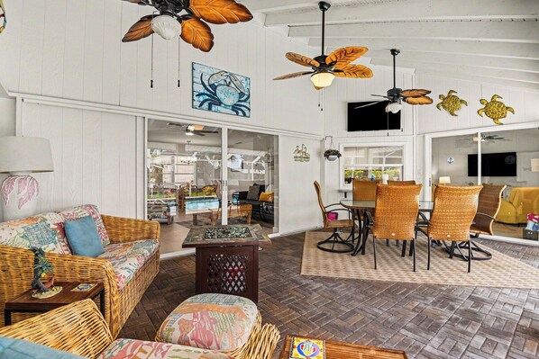 A room with wicker furniture, ceiling fans, and a large window. - Palaco Paradise - Waterfront Oasis with Large Pool (Cape Coral)