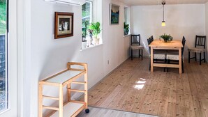 A room with a wooden floor, a dining table with chairs, a small wooden shelf, and a window with a view of greenery. - Lovely home in Gistrup with WiFi (Gistrup)