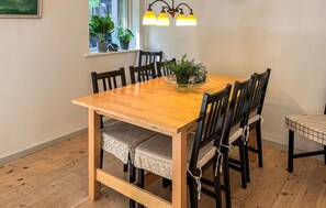 A dining table with six chairs, a window with plants, and a wall-mounted light fixture.