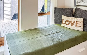 A bed with a green textured mattress, a pillow with 'LOVE' embroidered in brown, and a window with a view of a wooden deck.