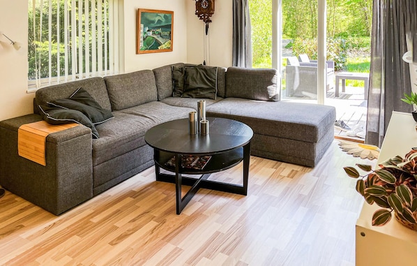 A modern living room with a sectional sofa, a round coffee table, and large windows offering a view of the outdoors.