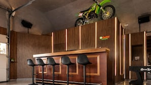 Eine Barbereich mit einer Holztheke, schwarzen Barhocker und einem an der Decke befestigten Motorrad.