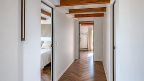 Ein Flur mit Holzboden, einem Bett mit weißer Bettwäsche und einem Kleiderständer aus Metall.