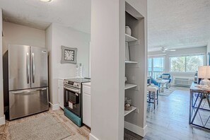 Een moderne keuken met roestvrijstalen apparatuur, een eethoek met tafel en stoelen, en uitzicht op het buitengebied door grote ramen.