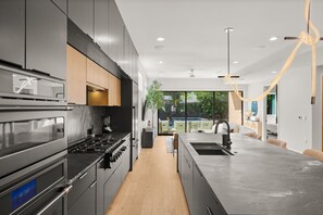 Eine moderne Küche mit Backofen, einer großen Kochinsel inklusive Spüle und Blick auf eine Terrasse.