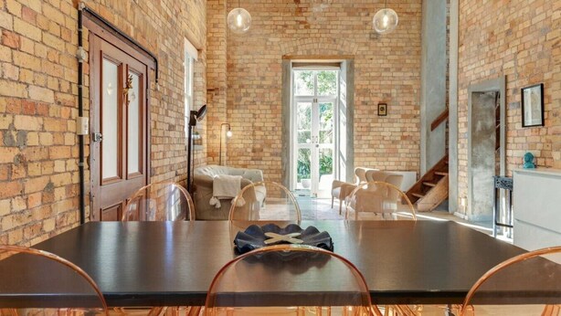 Un comedor con pared de ladrillo, una mesa grande y sillas transparentes.