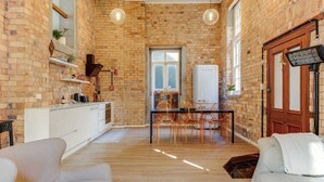 Una habitación con pared de ladrillo, sofá blanco, mesa de comedor con sillas y un armario blanco.