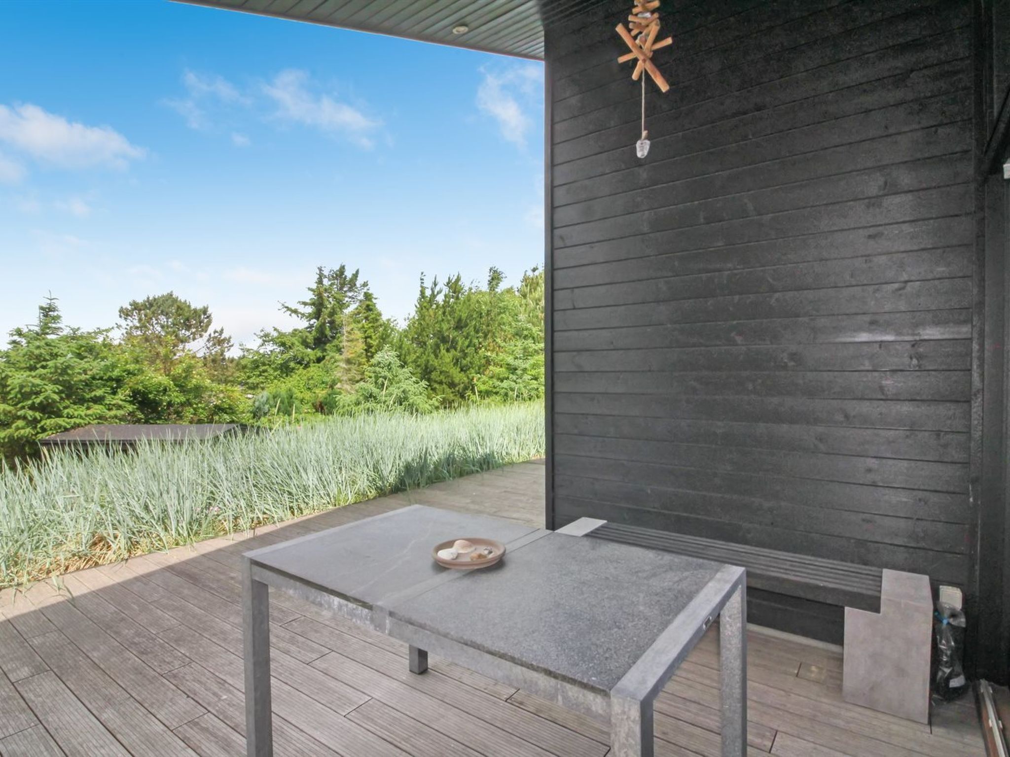 Une terrasse extérieure avec une table et des chaises, entourée d’une plateforme en bois et d’un mur noir.