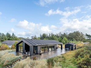 Una casa moderna con una terraza amplia, un garaje y un cobertizo pequeño en un entorno natural.