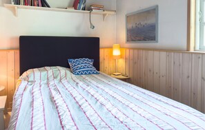 Ein Bett mit gestreifter Decke, eine Nachttischlampe, ein Nachttisch und ein Regal mit Büchern.