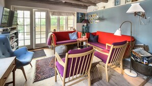 Una sala de estar acogedora con un sofá rojo, sillas azules, una mesa de madera y un ventanal grande.