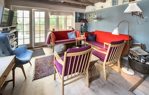 Ein gemütliches Wohnzimmer mit einem roten Sofa, blauen Sesseln, einem Holztisch und einem großen Fenster.