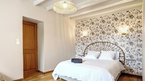 Ein Schlafzimmer mit Holztür, einem Bett mit weißer Bettwäsche, floralem Wandpapier und einem einzigartigen Kopfteildesign.