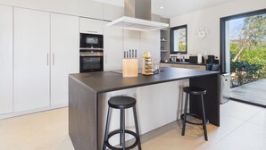 A modern kitchen with a central island, bar stools, a built-in oven, and a large window.