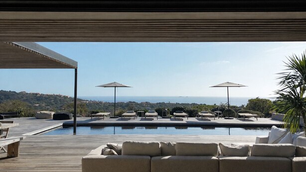 A poolside area with lounge chairs, umbrellas, and a view of the sea.
