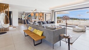 A modern living room with a sofa, a hanging chair, a dining area, and a view of the outdoors.