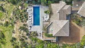 An aerial view of a house with a swimming pool, outdoor seating, and a landscaped garden.