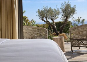 Ein Hotelzimmer mit einem Bett, Korbstühlen und Blick auf Olivenbäume und viel Grün.