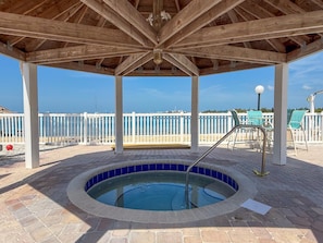 A covered outdoor swimming pool with a wooden roof, a white fence, and a view of the sea. - Cozy St. Pete Condo |  Pool | Near Beaches (St. Petersburg)