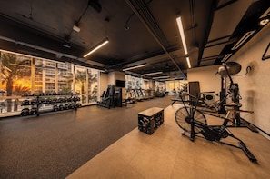 Ein Fitnessraum mit Trainingsgeräten, großen Fenstern und Blick auf Palmen.