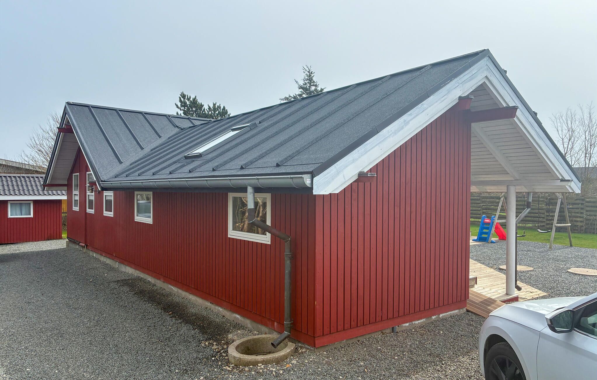 A red building with a sloped roof, a small attached structure, and a gravel driveway.