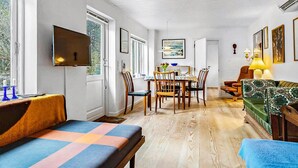 A room with a TV, dining table, chairs, a sofa, and artwork on the walls.