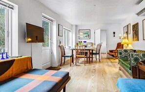 Ein Zimmer mit Fernseher, Esstisch, Stühlen, einer Couch und Kunstwerken an den Wänden.