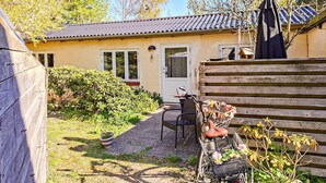 A house with a tiled roof, a door, and a window. There is a bicycle with a basket and a chair outside.