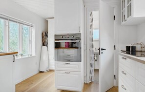 Eine Küche mit weißen Schränken, einem eingebauten Backofen und einem Fenster mit Blick auf Bäume.
