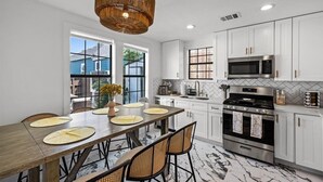 A modern kitchen with white cabinets, a large dining table, and a hanging light fixture. - Blue Haven | Hot Tub, Fire Pit & Outdoor Oasis (Galveston)