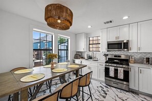 Une cuisine moderne avec des meubles blancs, une grande table à manger et un luminaire suspendu.