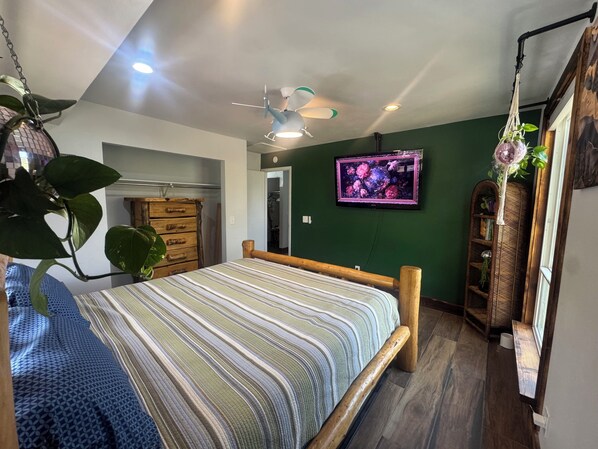 Een slaapkamer met een bed, houten hoofdbord, plafondventilator, groene wanden en een televisie aan de muur.