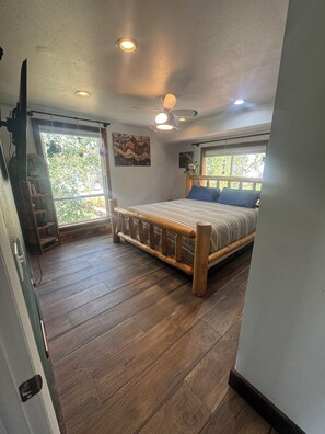 Un dormitorio con cama de madera, ventilador de techo y ventana grande.