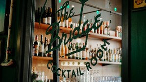Un bar avec des étagères remplies de bouteilles d’alcool et de verres, et une enseigne indiquant : « The Bridge Cocktail Room ».