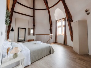 Une chambre à coucher comprenant un lit, une table de chevet, une lampe, un miroir, une fenêtre et des poutres en bois.